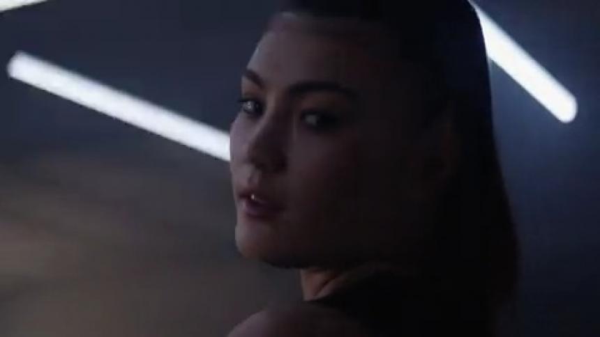 An asian woman stands in a room and casts a come hither look