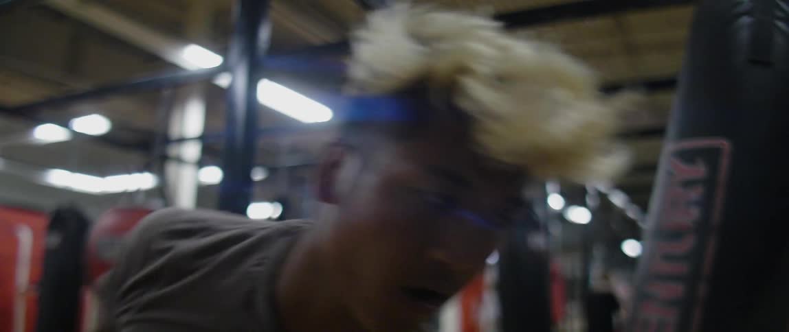 Black man wearing boxing gloves punches a punching bag at the gym