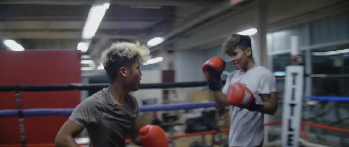 Two teens punch in a boxing room as people watch them