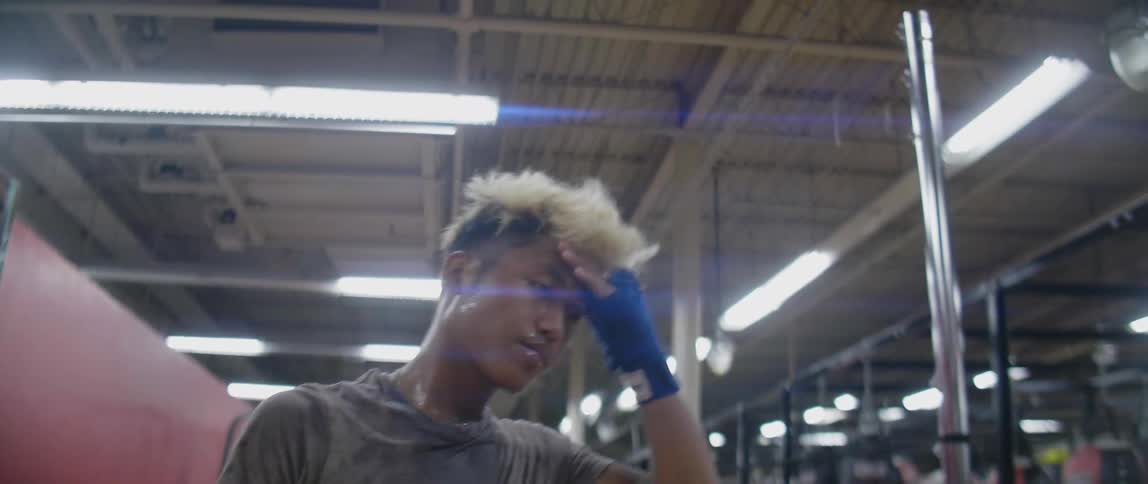 An asian male drenches his face with water and then walks through a gym