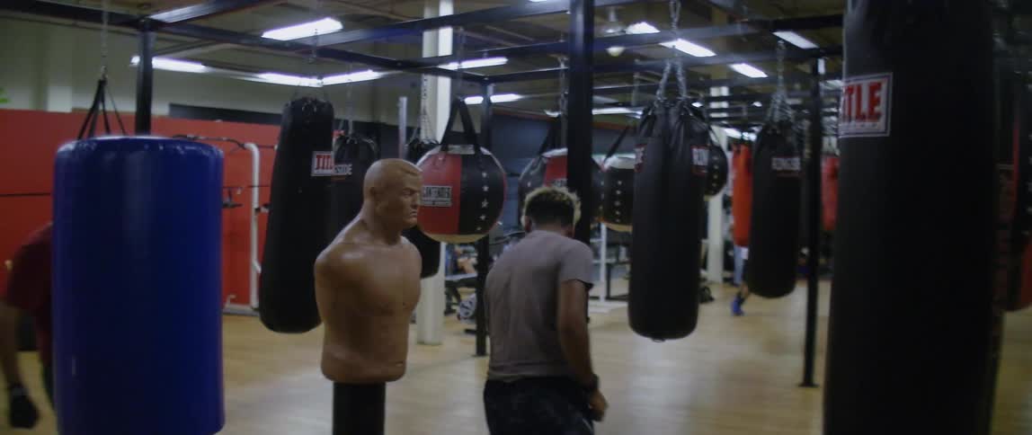 A man exercises by dodging through a row of punching bags at a gym