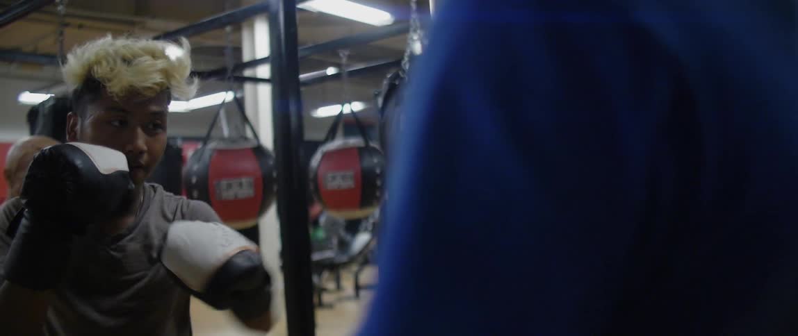A man punches the heavy bag held by a sparring partner