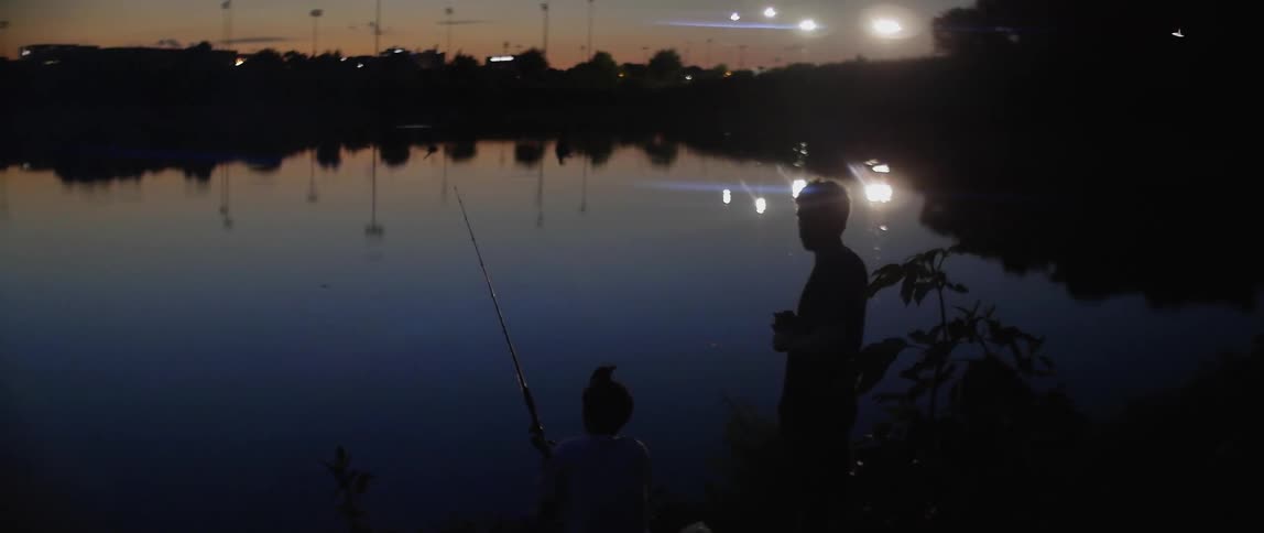A silhouette of boys fishing by the lake at dusk