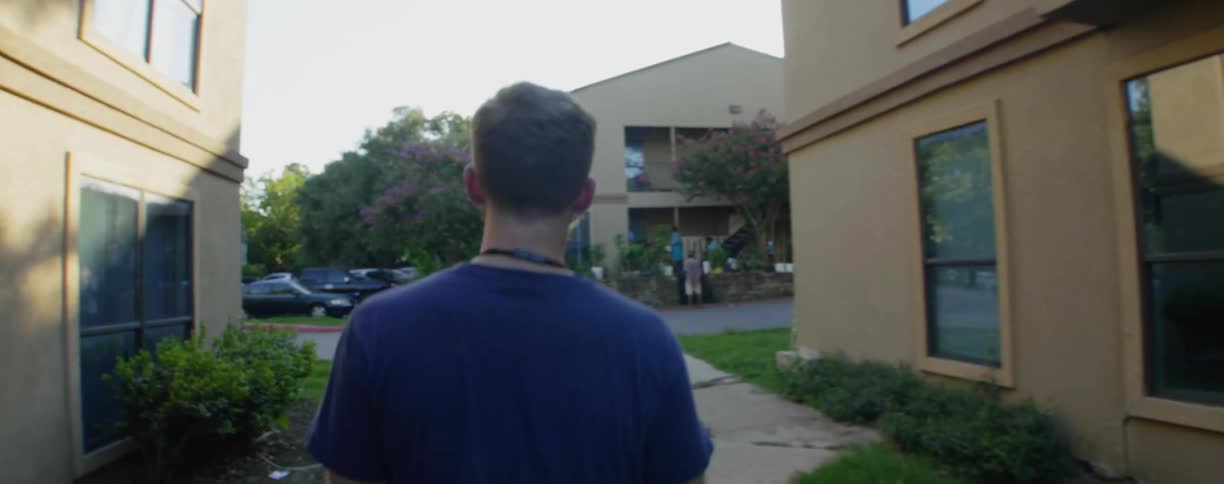A young man walks by an apartment building towards the parking lot