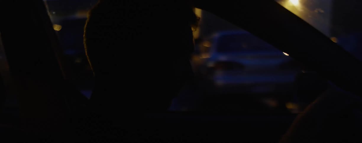 A white male drives a car through an urban area