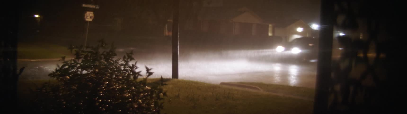 A car drives through a neighborhood intersection during a heavy rainstorm