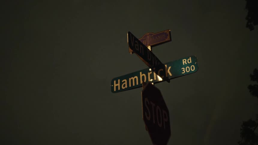 Lightning flashes in a cloudy sky behind a pole with street signs and a stop sign