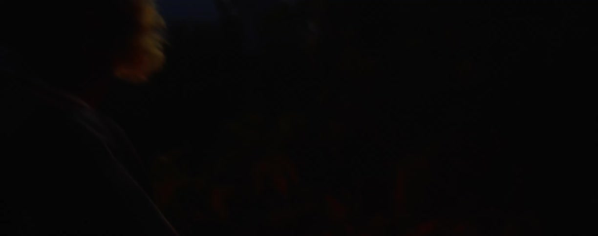 An asian male breaks sticks and feeds a small campfire on the shores of a lake at dusk