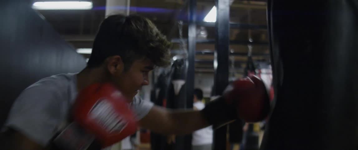 Young man practices boxing on a punching bag in gym