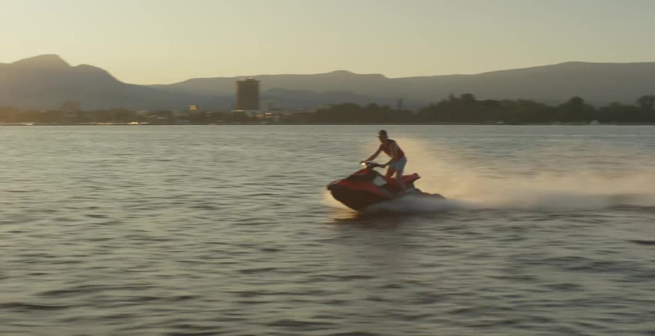 Male standing while driving a jet ski across the lake leaving a wake of water behind him