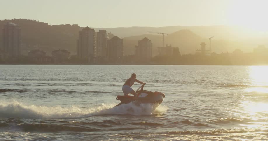 A man rides a jet ski in a bay near a coastal city