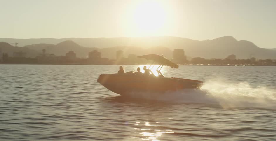 A speed boat with three passengers zips across a body of water off the coast of a city