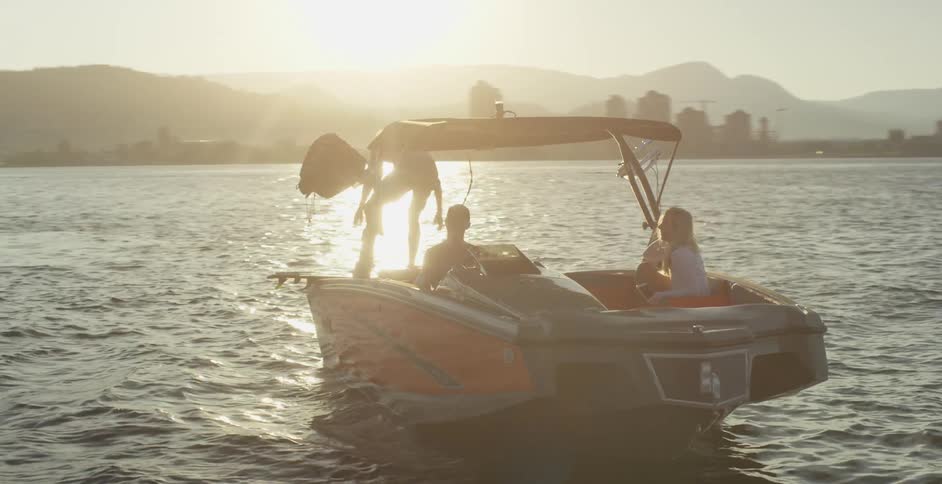 Man sets a body board at the back of a boat while two other people sit in the seats