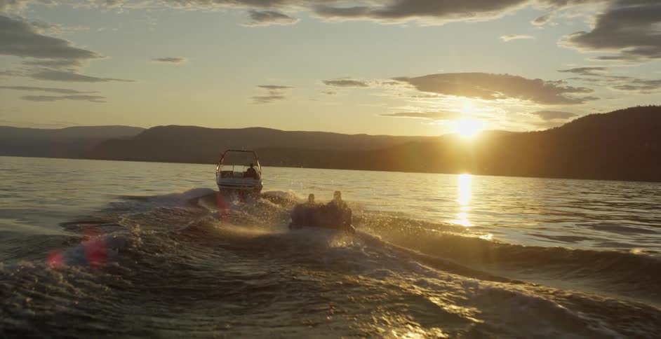 Boat towing people on a raft on a lake at sunset