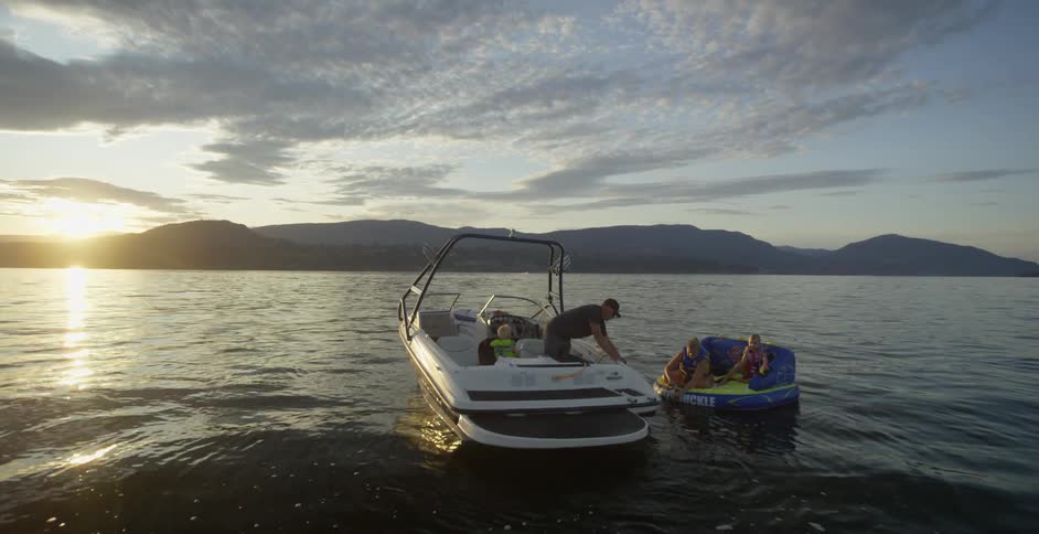 A man on a boat with a little boy helping a woman on a floating chair with a little girl unfurl the rope connecting the boat to the float