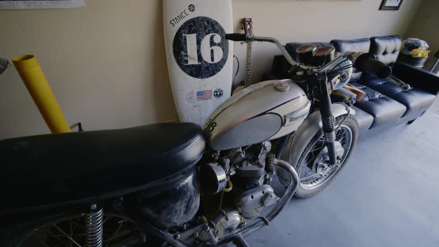 A surfboard and motorcycle sit inside a room with a couch