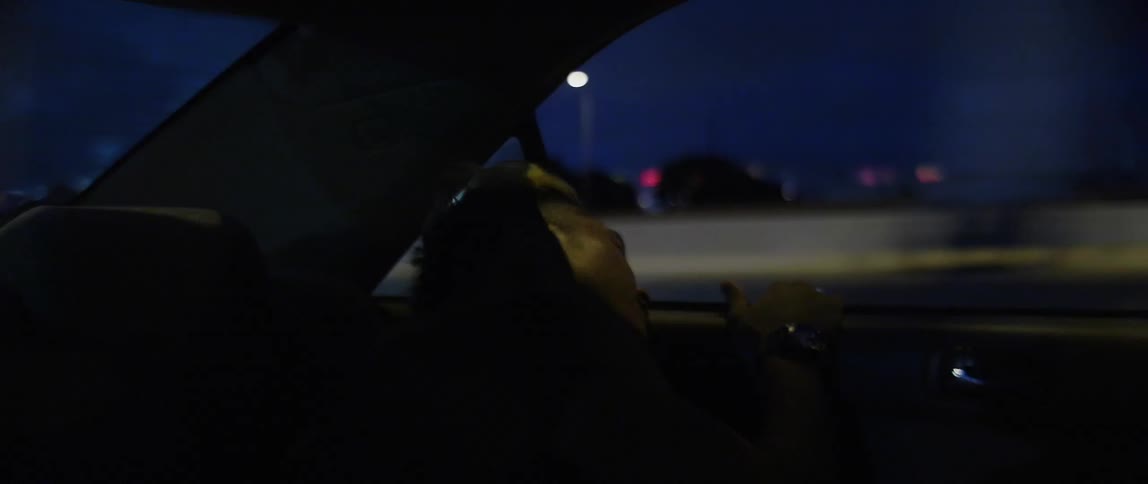 A man riding in the back seat of a car leans his head against the open window