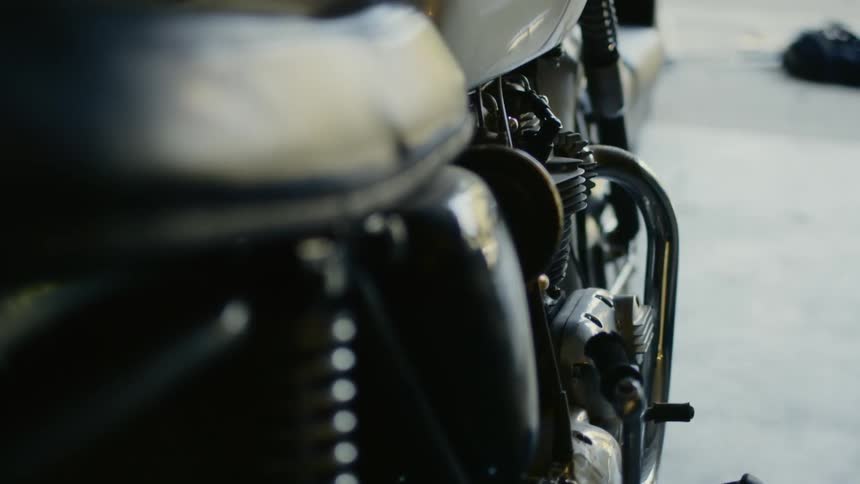 A motorcycle parked in a garage as a person picks up construction materials in the driveway