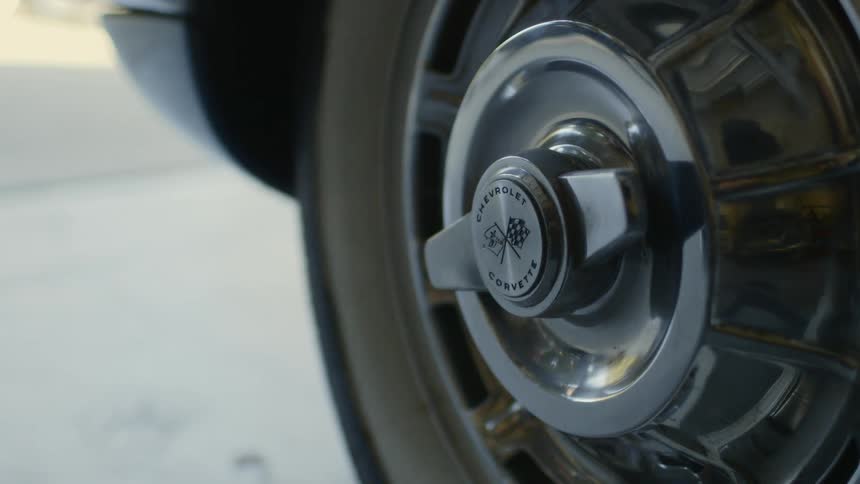 A teenagers reflection on a car tire as he walks by