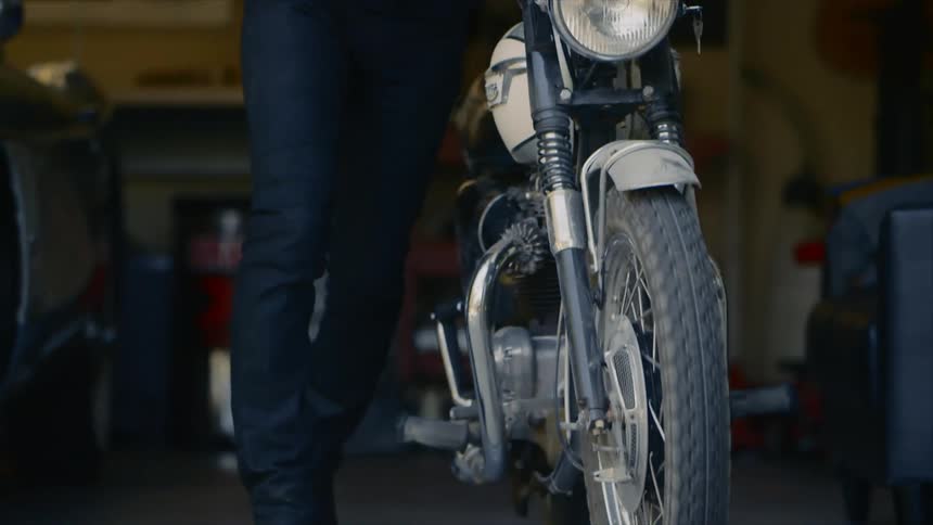 A person pushes their motorcycle out of the garage