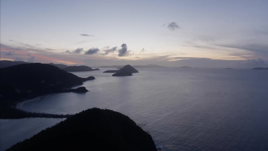 An islet sits off the coast of a land mass with mountains covered in forests