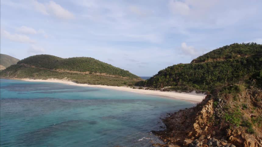 A beach sits in an ocean cove surrounded by hills and a mountain