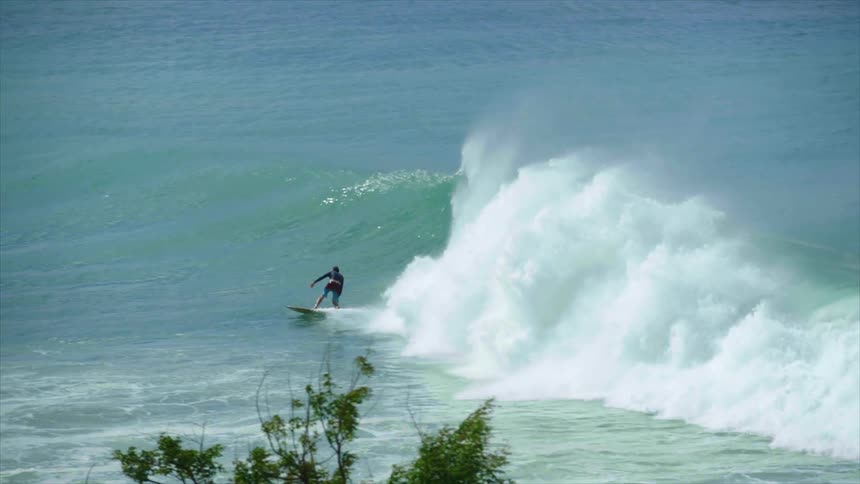 A surfer outruns and evades a crashing ocean wave on their surfboard