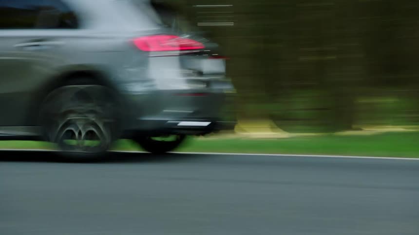 A car races down the highway near a large forest