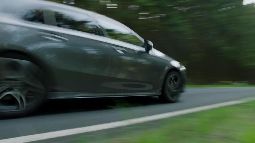 A car drives down a street past a forest