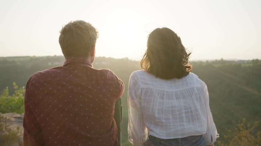 Man and woman sitting on the edge of the cliff watch sunset
