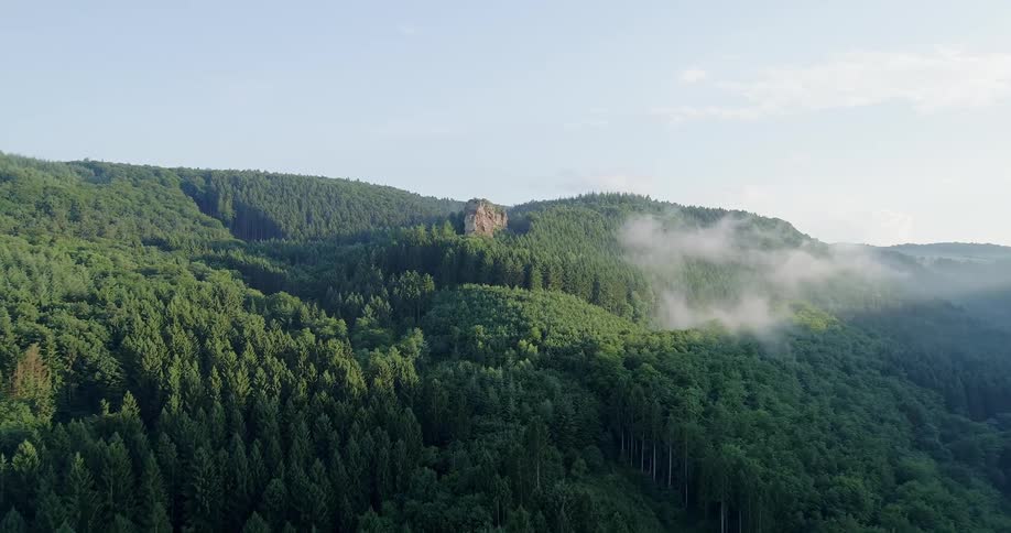 Wisps of a cloud hang over a forest that covers rolling hills