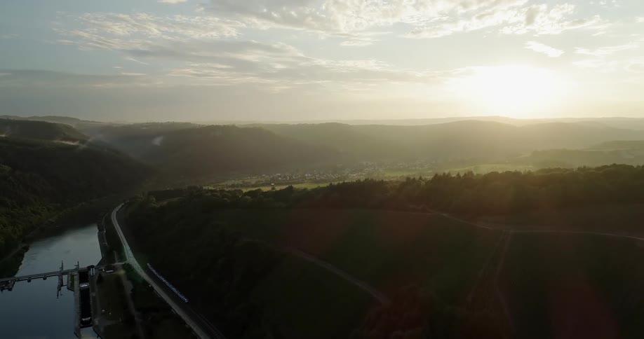 A aerial view of a train traveling alongside a river and a forest