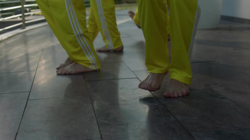 A group of people dance together in yellow track suit pants