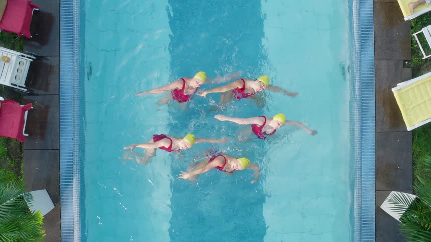 Aerial of synchronized swimmers in a narrow pool outdoors