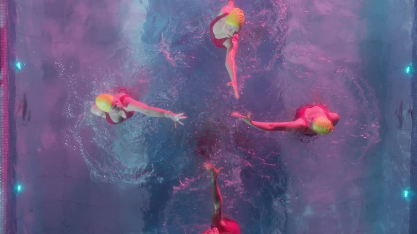 Five women synchronize swim in an outdoor pool at night