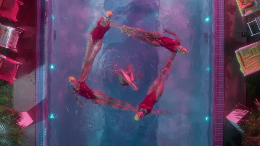 Five women practice synchronized swimming in an outdoor pool at night