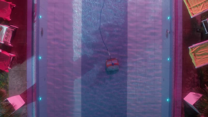 A robotic vacuum cleaner moves underwater cleaning the bottom of a large pool with deck chairs around