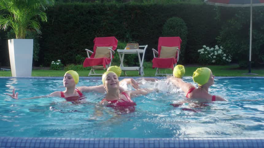Five women synchronize swim in an outdoor swimming pool