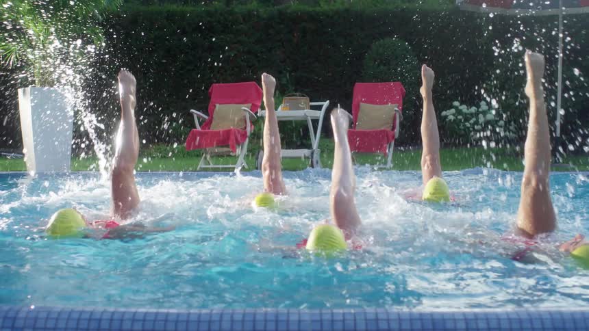 Five women kicks their legs in sync while swimming in a pool