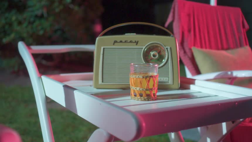 A vintage radio and a drink sit on a table next to a lawn chair
