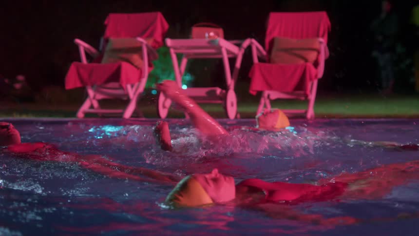 Women practice synchronized swimming in an outdoor pool at night