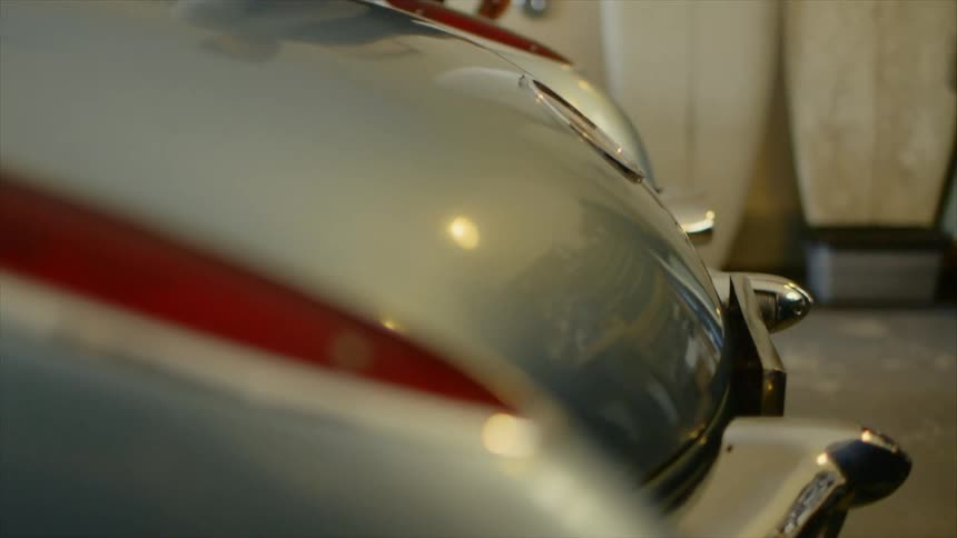 Two white men walk around the rear of a vintage car