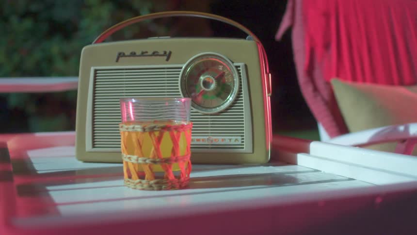 A retro radio sits on a table with an orange beverage in a glass