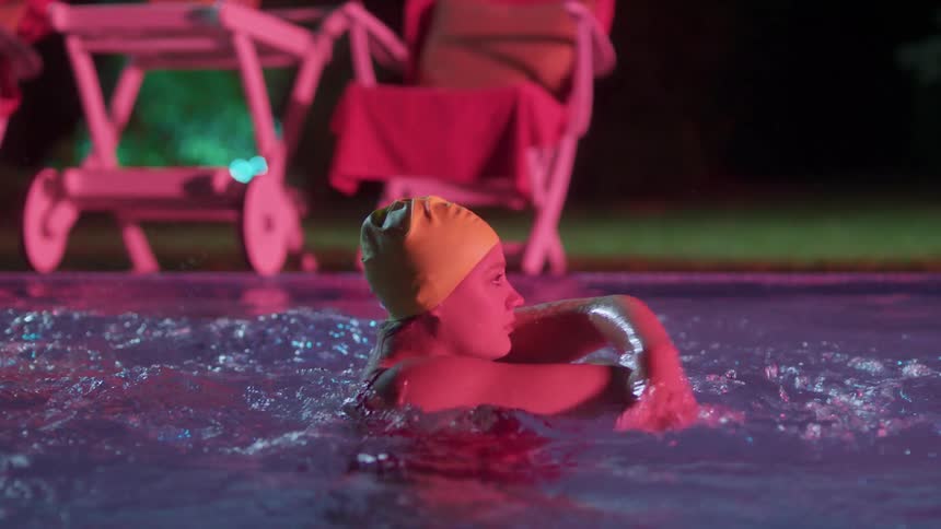 A group of female synchronized swimming performing a swimming routine in an outdoor pool at night