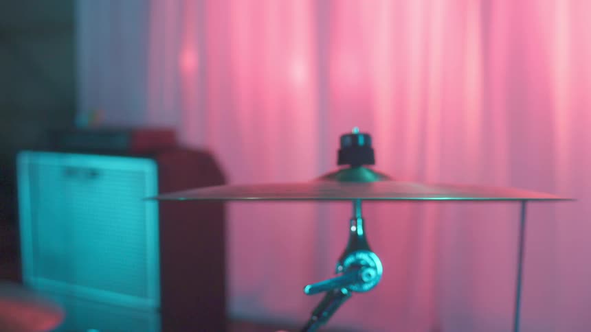 A drum cymbal and stand sit on a stage behind a closed curtain