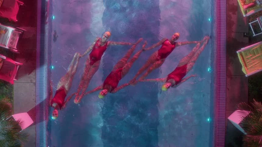 Synchronized swimmers floating in a narrow pool outdoors at night