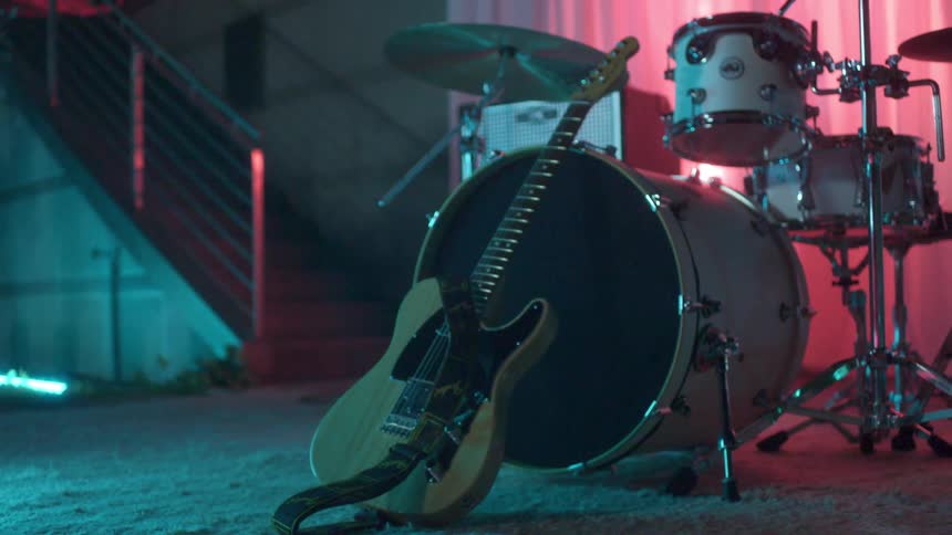 A guitar and drum set standing in a room dimly lit by red and blue lights