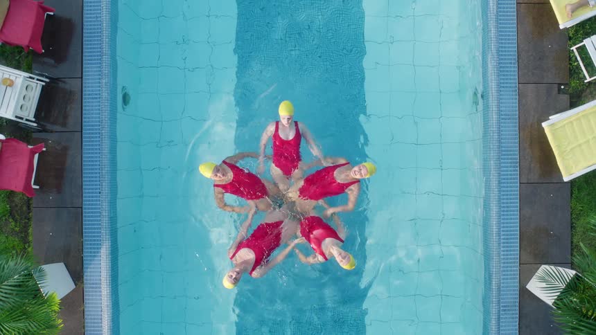 Five women synchronize swim in an outdoor pool