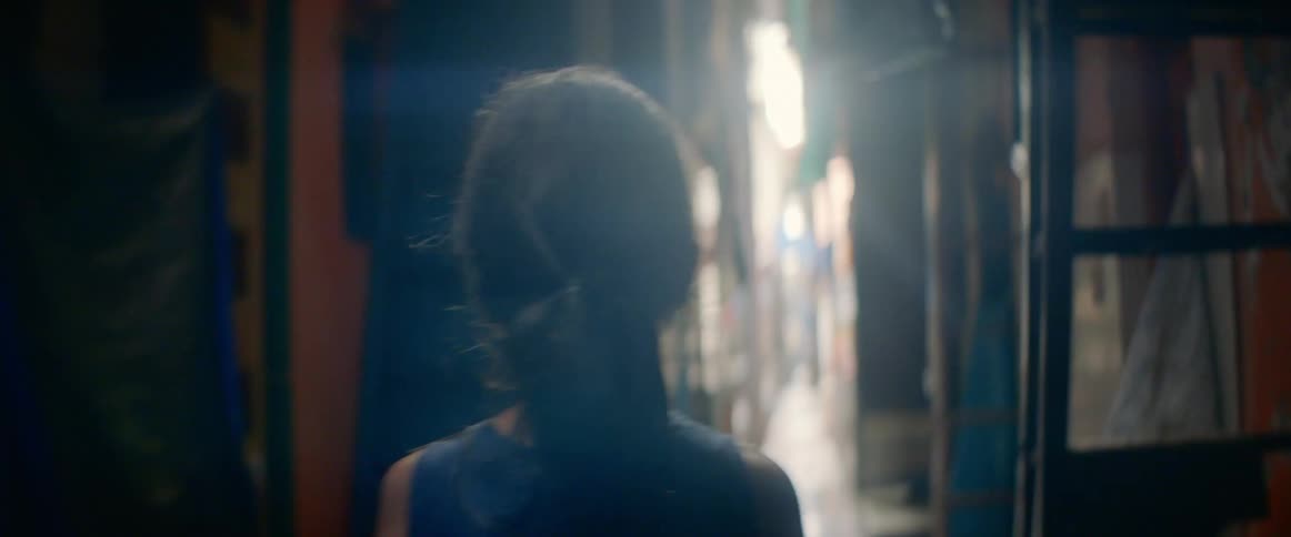 A young girl walks down a narrow alleyway filled with ladders and tight knit living units