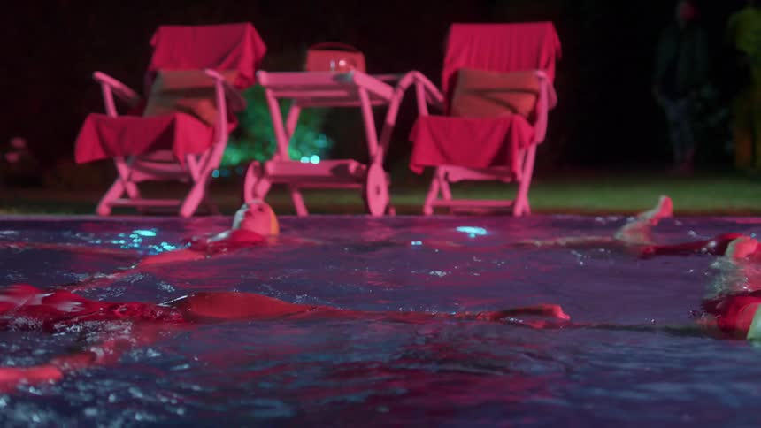 Five females wearing yellow swim caps and pink bathing suits perform a synchronized swim routine in a swimming pool at night